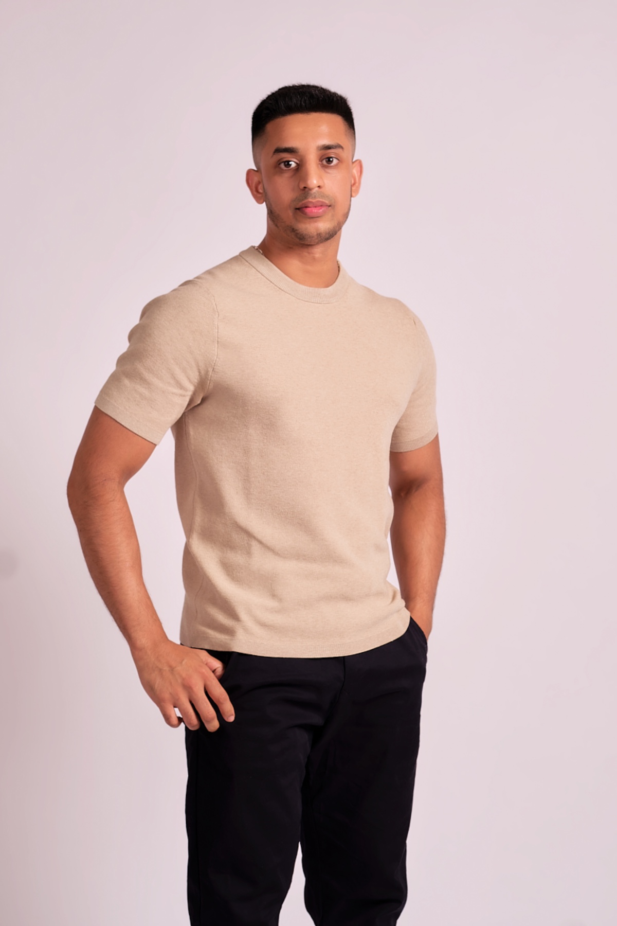 abdul-wadid-2 A man wearing a beige t-shirt poses confidently against a neutral light grey studio background.