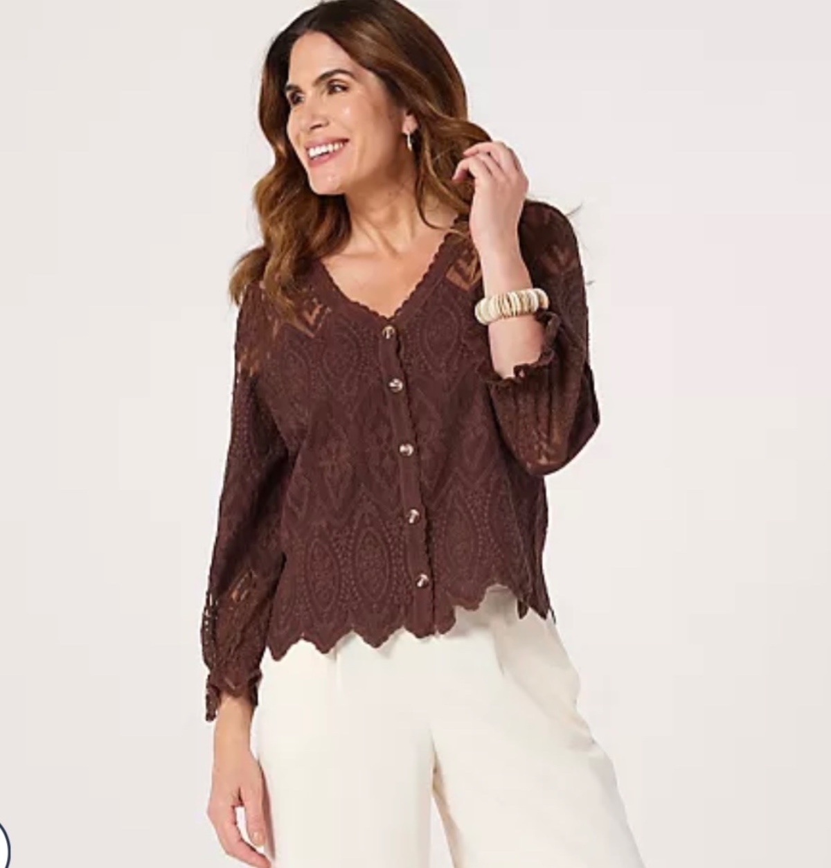 A smiling brunette woman wearing a brown lace blouse against a clean bright studio background.