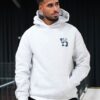 A handsome man wearing a grey panda-logo hoodie looks away while standing in a bright indoor studio.