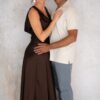 A well-dressed couple smiling warmly at the camera while standing together against a clean studio backdrop.