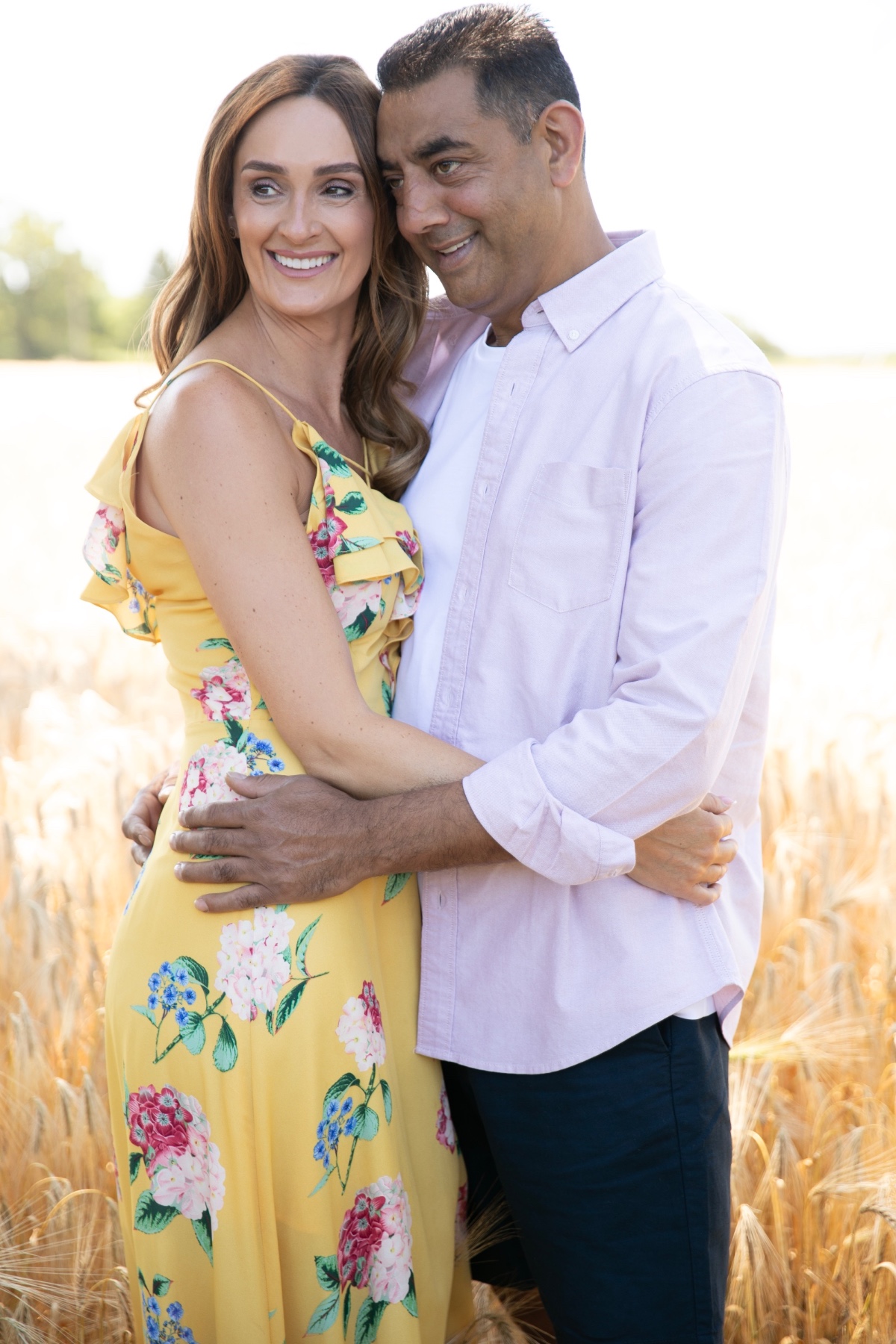 A happy diverse couple embraces in a bright, sun-drenched golden wheat field during a summer day.