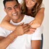 A happy diverse couple wearing casual white t-shirts smiles warmly against a clean, bright studio background.