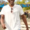 deondre-cumberbatch-7 A smiling man in a white polo shirt walks through a sunny, outdoor amusement park setting.