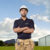 mohan-randhawa-13 A male worker wearing a branded hard hat and tool belt stands confidently in a grassy field.