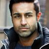 mohan-randhawa-10 A focused man with dark hair and stubble wears a dark jacket in this crisp headshot portrait.