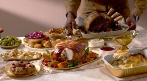 A person prepares a festive roast dinner spread featuring turkey, beef, and various seasonal side dishes.