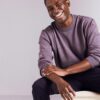 deondre-cumberbatch-3 A smiling Black male model wears a casual purple sweater against a clean, neutral studio background.