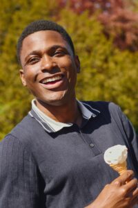 A smiling man holding an ice cream cone outdoors, looking friendly, warm, and relaxed in natural sunlight.