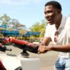 deondre-cumberbatch-9 A man wearing a white polo shirt laughs joyfully while playing a game at an outdoor fairground.