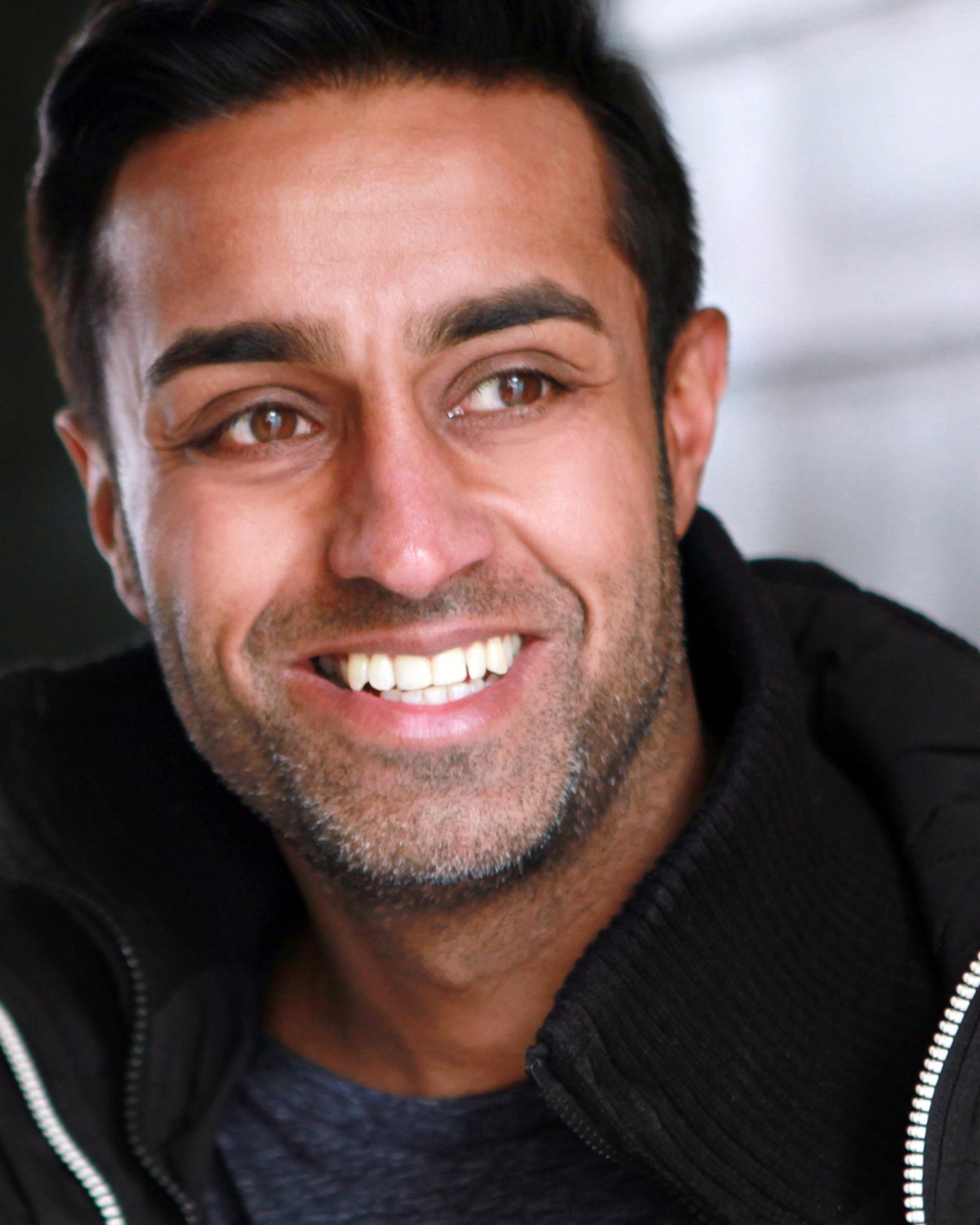 A friendly man with a warm, genuine smile looks off-camera in this bright and clean portrait shot.