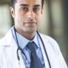 mohan-randhawa-4 A professional male doctor in a white coat and stethoscope looking directly at the camera with confidence.