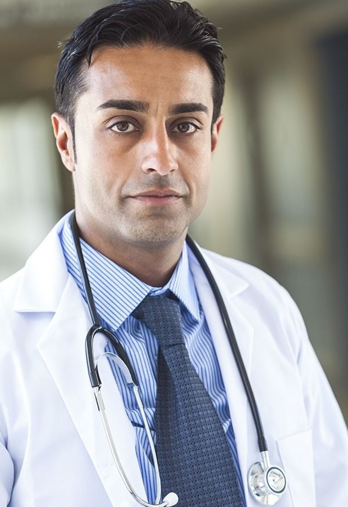 A professional male doctor in a white coat and stethoscope looking directly at the camera with confidence.