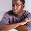 deondre-cumberbatch-4 A personable Black male model with short dark hair wears a purple sweater against a studio background.