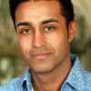 mohan-randhawa-5 A warm portrait of a man with dark hair wearing a blue patterned shirt against blurred greenery.