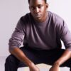 deondre-cumberbatch-2 A man wearing a mauve sweater sits against a plain background, looking directly into the camera lens.