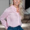 A blonde woman in a pink shirt smiling warmly, captured in a clean, brightly lit professional studio setting.