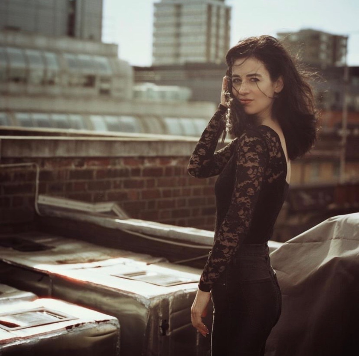 helena-antonio-7 A dark-haired woman in a black lace top poses on a city rooftop during a summer day.