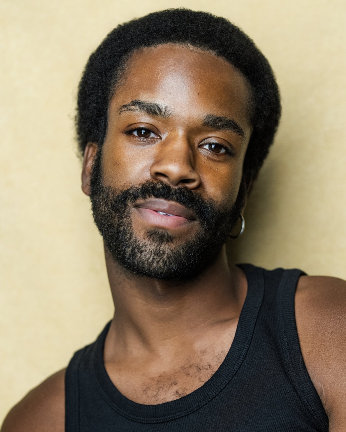 A warm portrait of a man with a beard, wearing a black tank top, against a golden background.