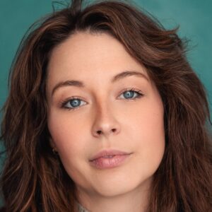 A headshot of a woman with long wavy brown hair against a textured teal studio background.