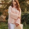 A woman wearing a cosy pink jumper and satin skirt stands outside in a golden autumn setting.