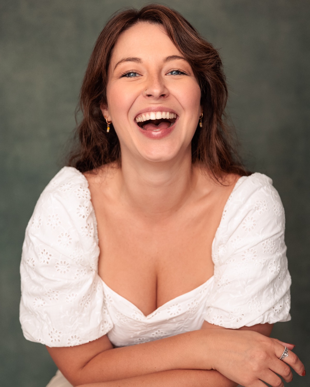 A cheerful brunette woman with a bright, genuine smile wearing a white blouse against a green background.