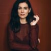 helena-antonio-6 A dark-haired woman with expressive eyes poses against a deep burgundy background in a professional headshot session.