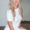 A smiling blonde woman wearing a simple white jumper, posing for a clean and professional studio headshot.