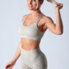 A blonde fitness model in a beige matching sports set posing against a clean grey studio background.