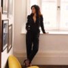 helena-antonio-8 A stylish brunette woman in a black jumpsuit leans against a window in a bright living space.