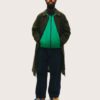 nathan-lobban-12 A stylish bearded man stands against a plain background wearing a green jacket, coat, and orange cap.