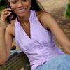 A smiling young woman with braided hair talks on her phone while sitting on a wooden bench.