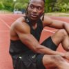 tobi-thomas-9 A fit male athlete in sportswear sits on a running track looking away with a focused expression.