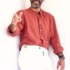 A smiling middle-aged man in a terracotta linen shirt poses playfully against a bright white wall.