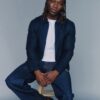 tobi-thomas-5 A stylish young man with braided hair sits on a wooden stool against a neutral studio backdrop.