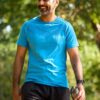 A smiling middle-aged man in a blue sports t-shirt walks outdoors, holding a water bottle after exercising.