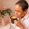 A woman enjoys a warm cup of coffee with a heart design in a bright, cozy setting.