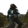 tobi-thomas-6 A man wearing a patterned fleece and sunglasses stands on a rocky mountain path in the hills.