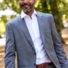 A smiling middle-aged man in a professional grey suit stands outdoors, exuding a friendly and approachable vibe.