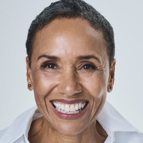 A warm, smiling mature woman with short hair wearing a crisp white shirt against a neutral background.