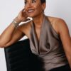 A sophisticated woman with a short haircut poses elegantly in a satin halter top against white background.