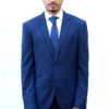 A man wearing a smart navy blue suit and tie stands against a plain white background.