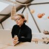 eloise-skinner-2 A woman with glasses works on a laptop in a bright, modern, airy loft style space.