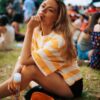 eloise-skinner-5 A blonde model sits on grass at a festival, holding a Bristows hair product with bright branding.