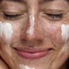 freya-wilson-3 A close-up of a smiling woman with natural freckles applying white skincare cream to her healthy face.